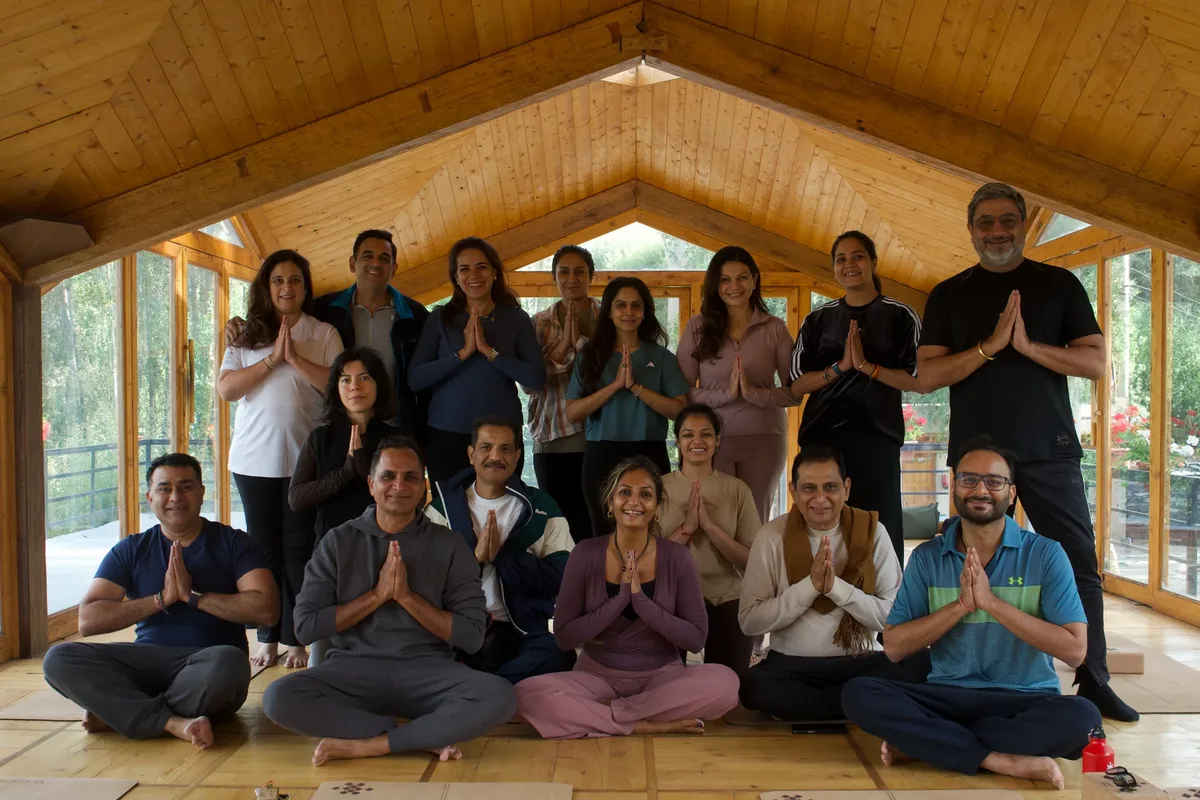 A group of people are sitting on the floor in a room, praying and smiling.