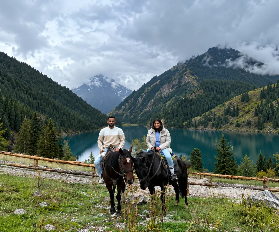 A man and woman are riding horses on a trail near a lake.